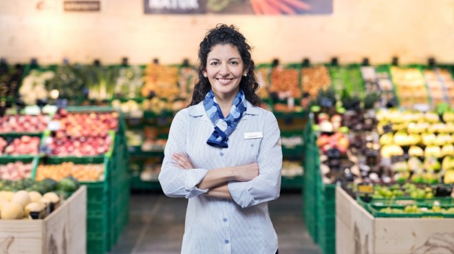 Eine Coop-Verkäuferin steht vor dem Obst- und Gemüseregal in einem Coop-Supermarkt.