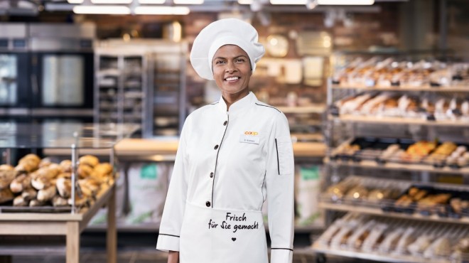 Eine Bäckerin vor der Bäckereiabteilung des Coop-Supermarktes lächelt in die Kamera.