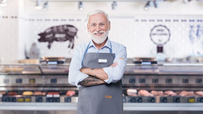 Ein Metzger vor der Fleischtheke in einem Coop-Supermarkt verschränkt die Arme und lächelt in die Kamera.