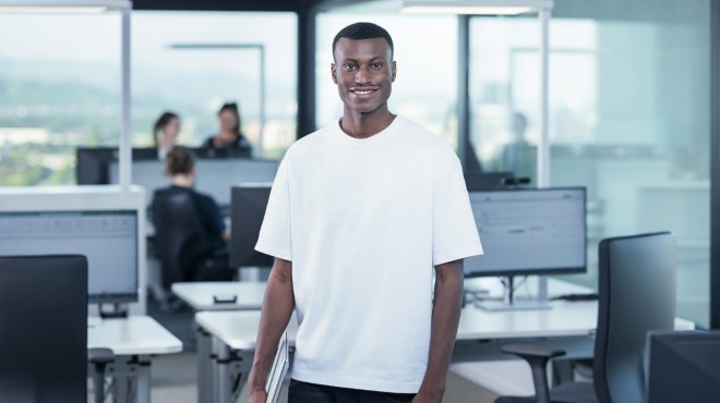 Un employé du service informatique dans son bureau, un ordinateur sous le bras, sourit à la caméra.