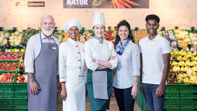 Un gruppo di collaboratrici e collaboratori Coop sorride all'obiettivo di fronte al reparto Frutta & Verdura di un supermercato Coop.