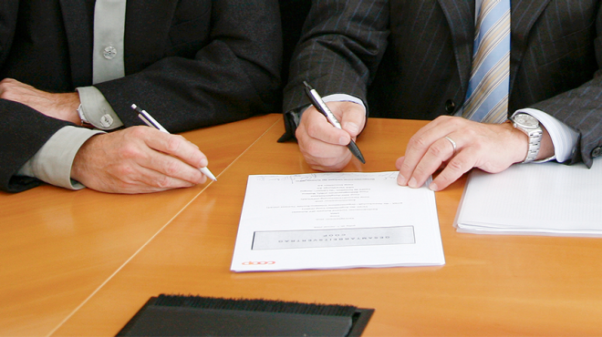 Due persone firmano il contratto collettivo di lavoro Coop stampato.