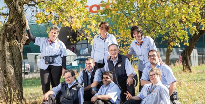 Otto dipendenti Coop in tenuta da lavoro su un prato con un albero davanti a un negozio Coop.
