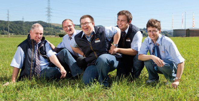 Cinque sorridenti dipendenti Coop in tenuta da lavoro su un prato.